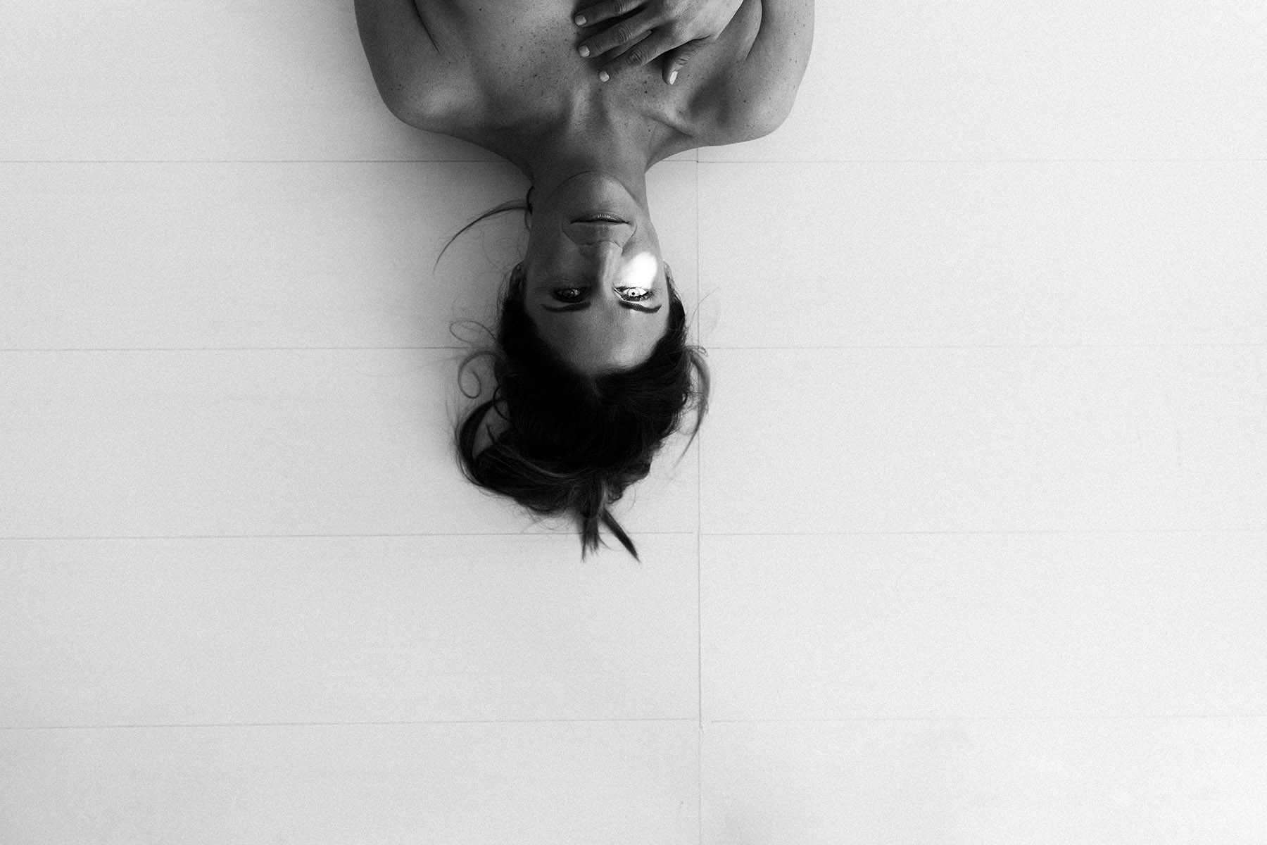 black and white image of a woman laying on a white studio floor during a session with Laurie Baker