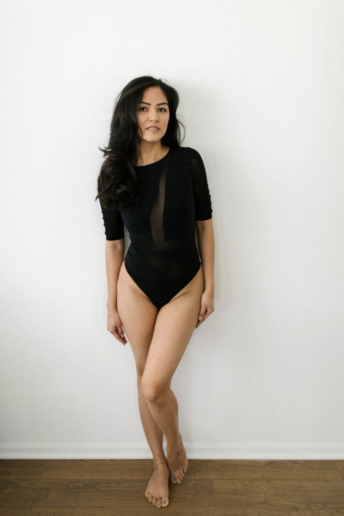 a woman leaning against a wall at photography studio wearing a one piece outfit 